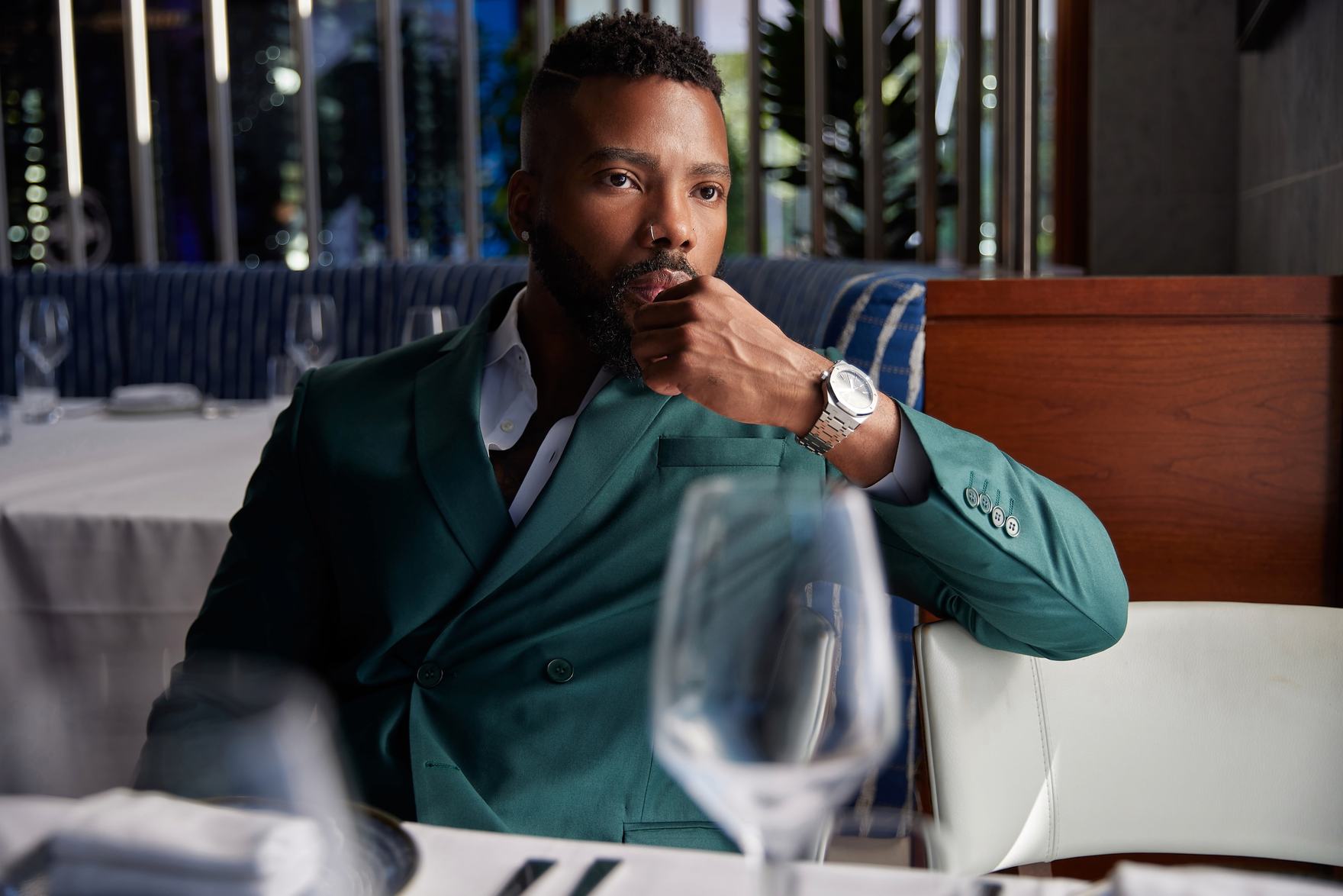 Sike Akhionbare seated at a restaurant table in an emerald double-breasted suit