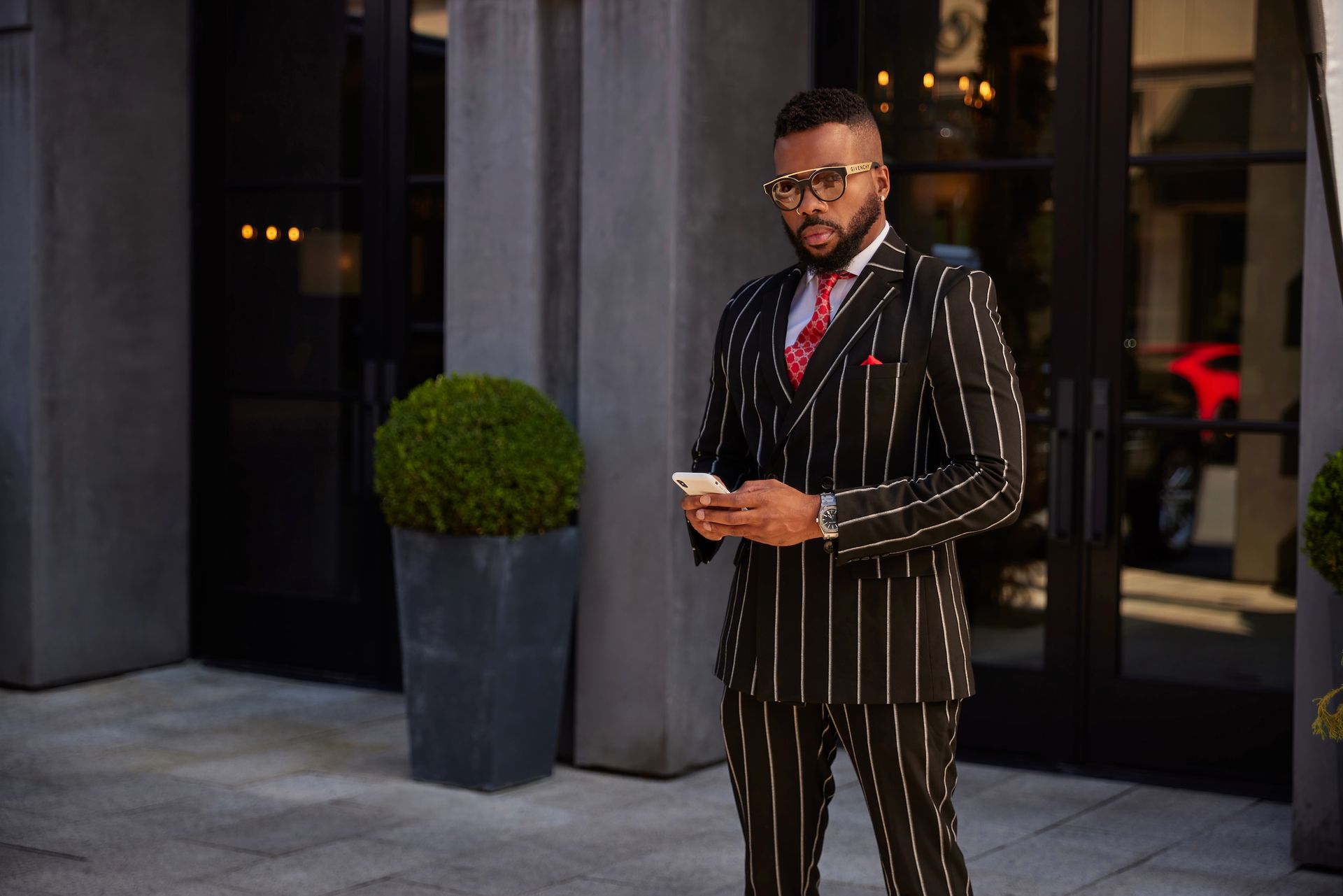 Sike Akhionbare in a black pinstripe suit and red silk tie outside a Houston building